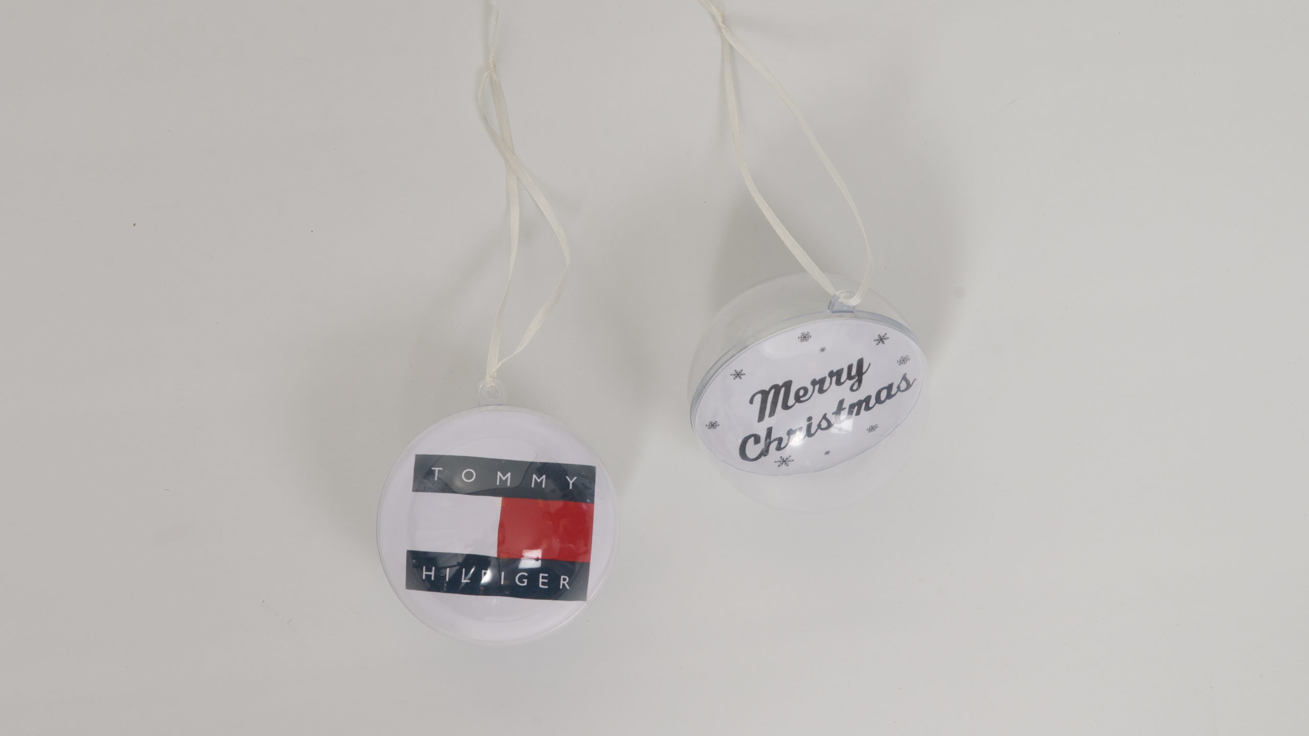 Zwei Plastkschneekugeln. eine Gebrandet mit Tommy Hilfiger und auf der anderen steht Merry Christmas.